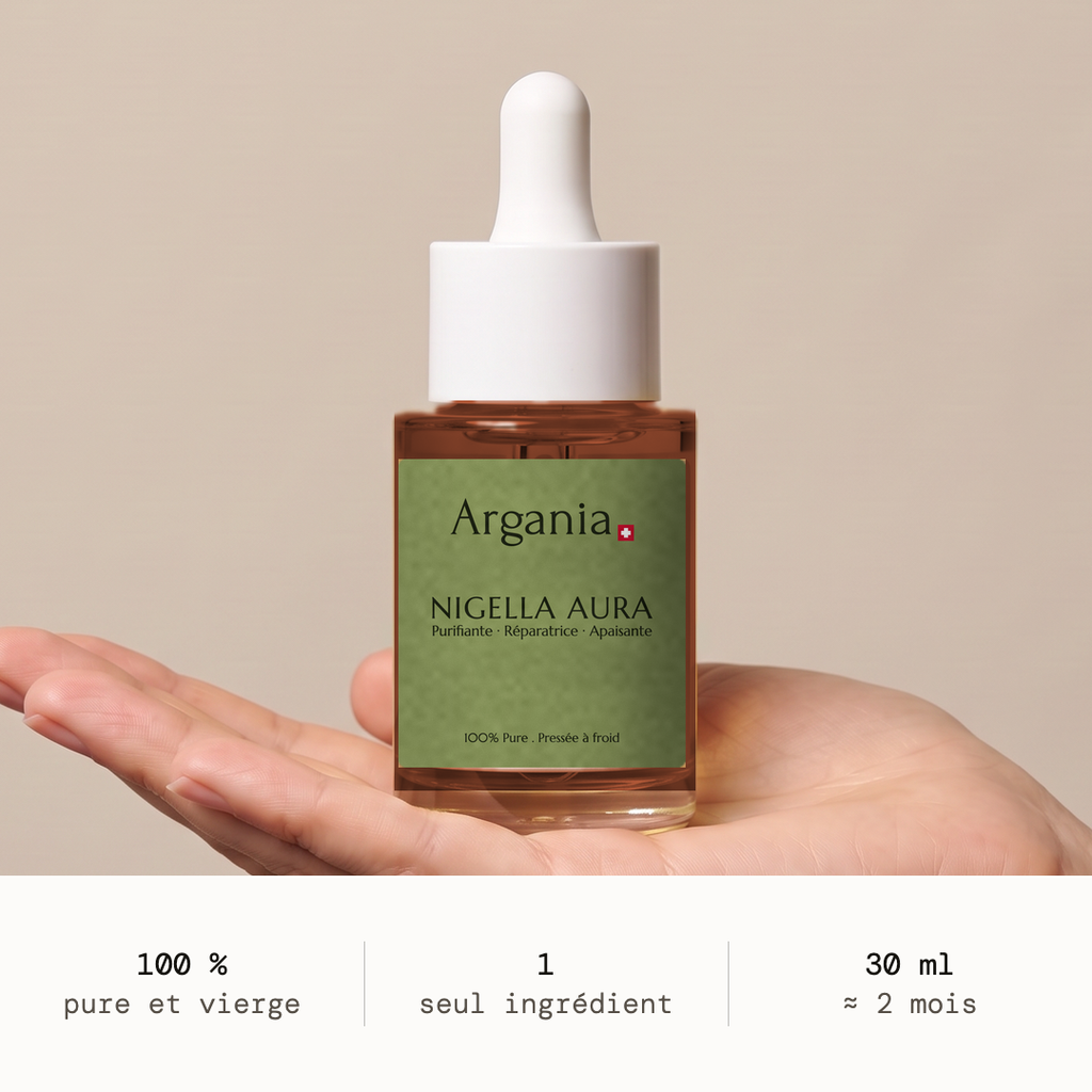 Flacone di olio di nigella Nigella Aura® Argania, 30 ml, presentato su una mano aperta su sfondo color taupe